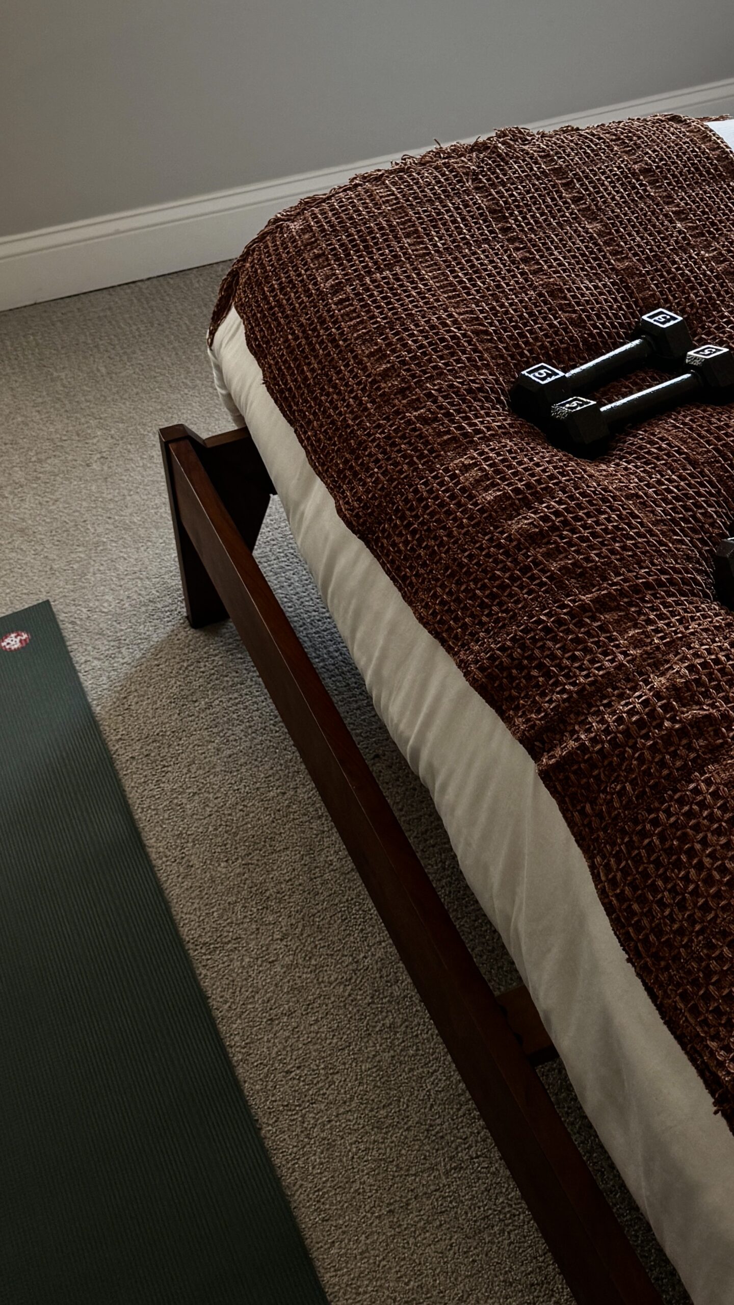 Weights on a bed next to a yoga mat on the floor
