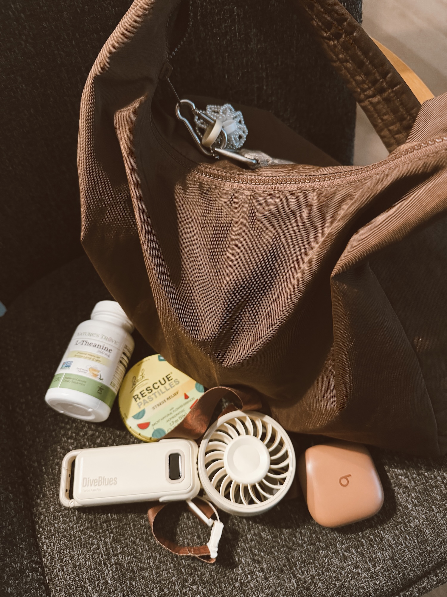 My anxiety bag contents spilled out next to a brown tote: L-theanine, Rescue Remedy pastilles, a handheld fan, and Beats earbuds.